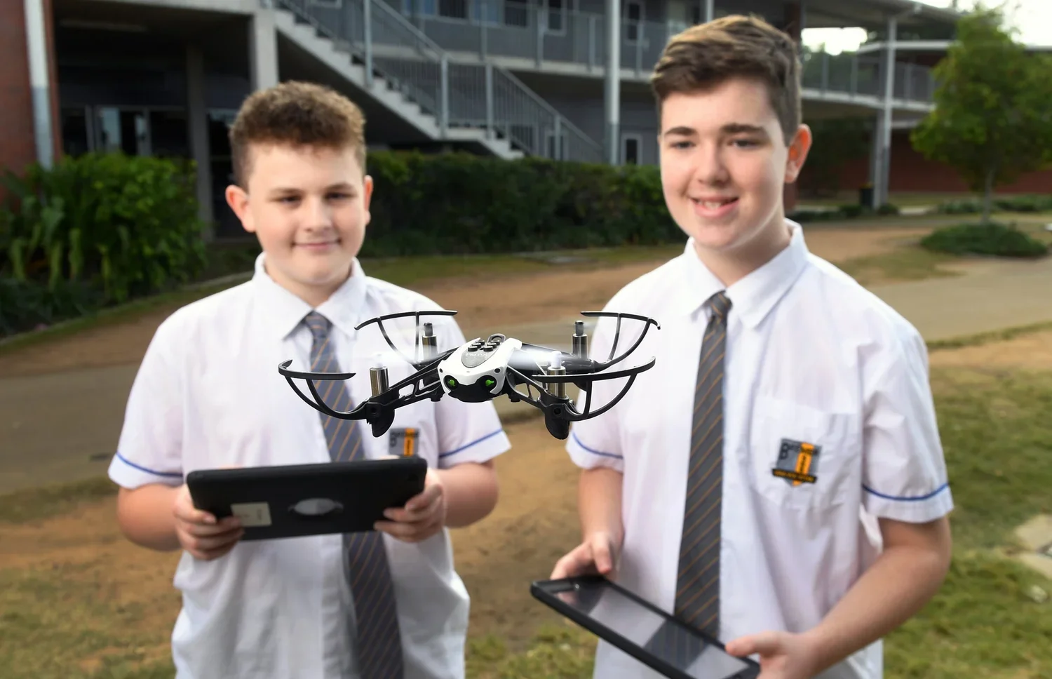 Two boys in school uniforms flying a drone outdoors with a tablet and remote control. School and Education Marketing Photography
