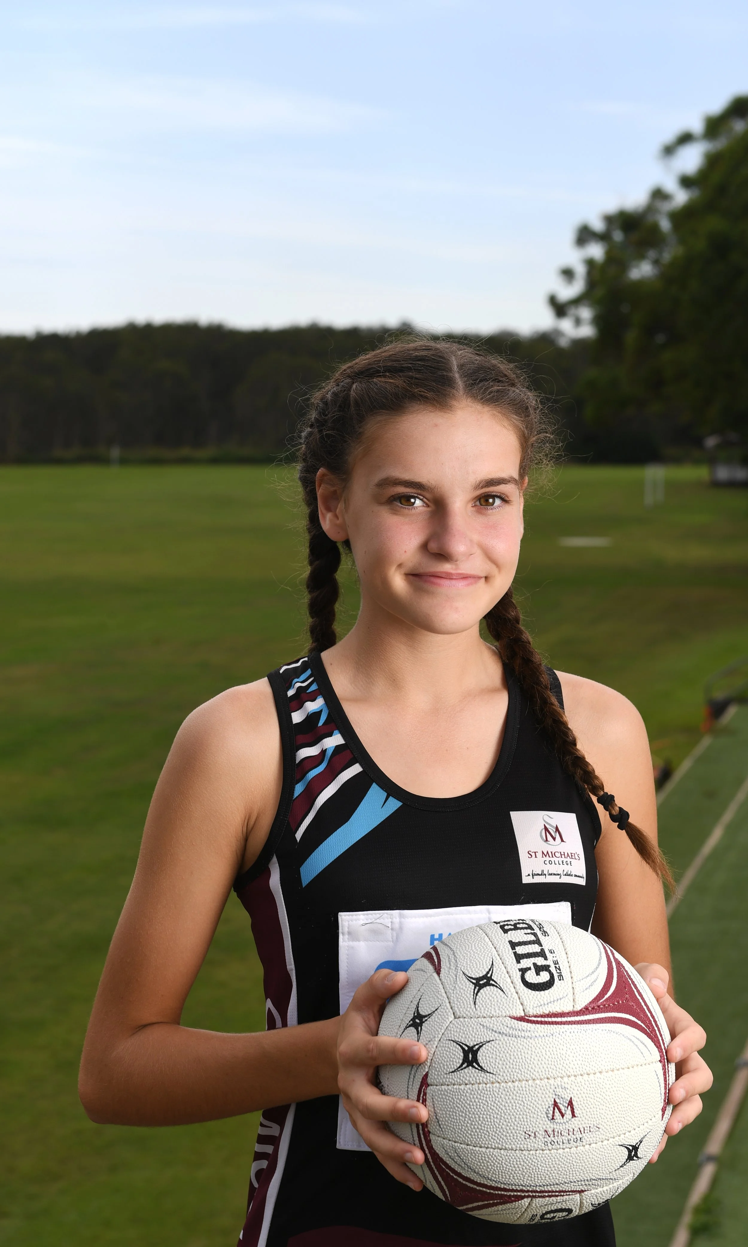 Young girl in sports uniform holding a volleyball outdoors on a grassy field.