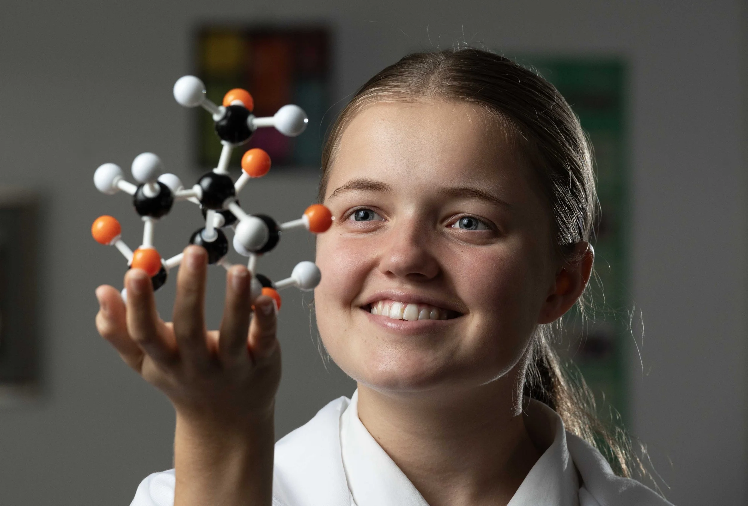 A young girl holding a molecular model in her hand, smiling and looking at it with interest. School and Education Marketing Photography