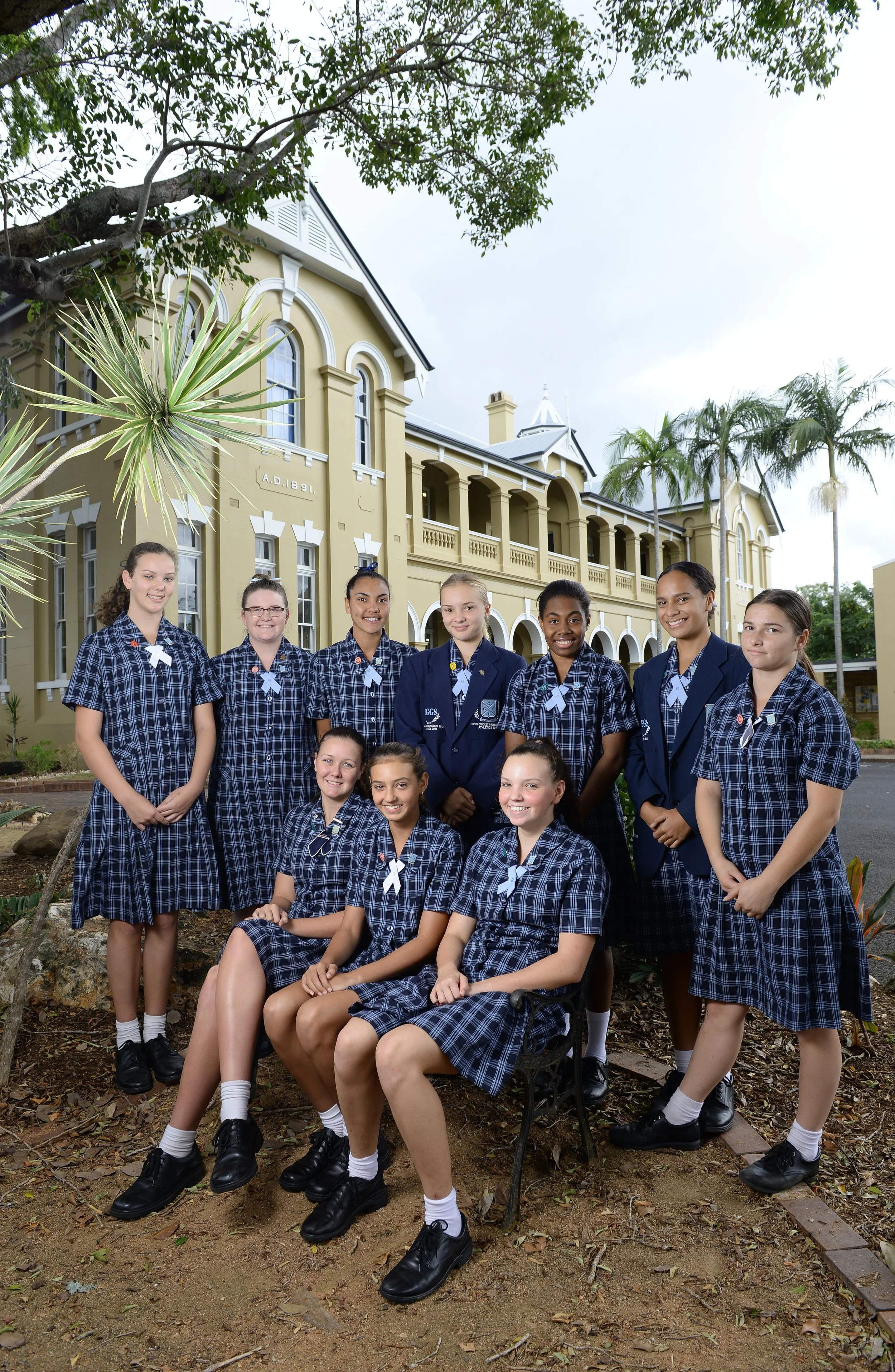 Group of schoolgirls in uniform posing outdoors in front of a yellow historical building with arched windows and palm trees. School and Education Marketing Photography
