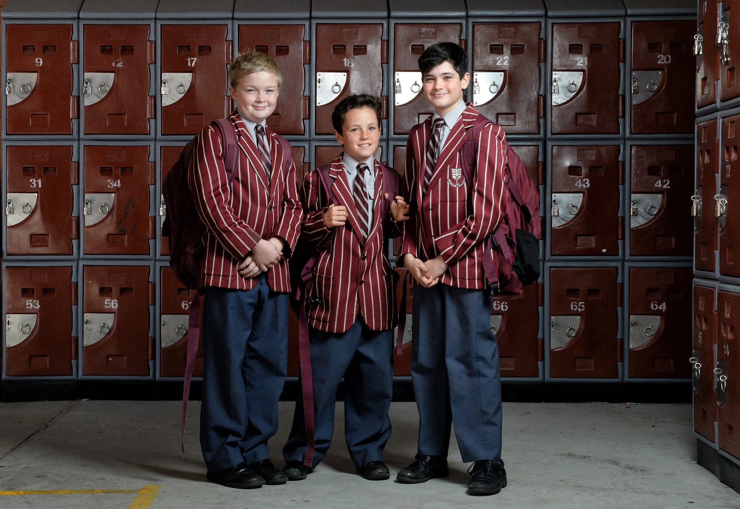 Three boys in school uniforms standing in front of lockers in a school hallway. School and Education Marketing Photography