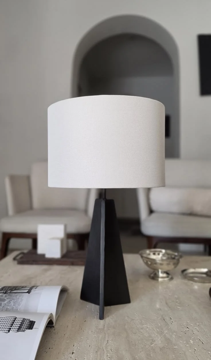 A modern table lamp with a black triangular base and a white cylindrical shade, a modern and simple statement.