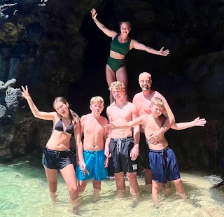 Group of five people in swimwear posing in shallow water outside a cave.