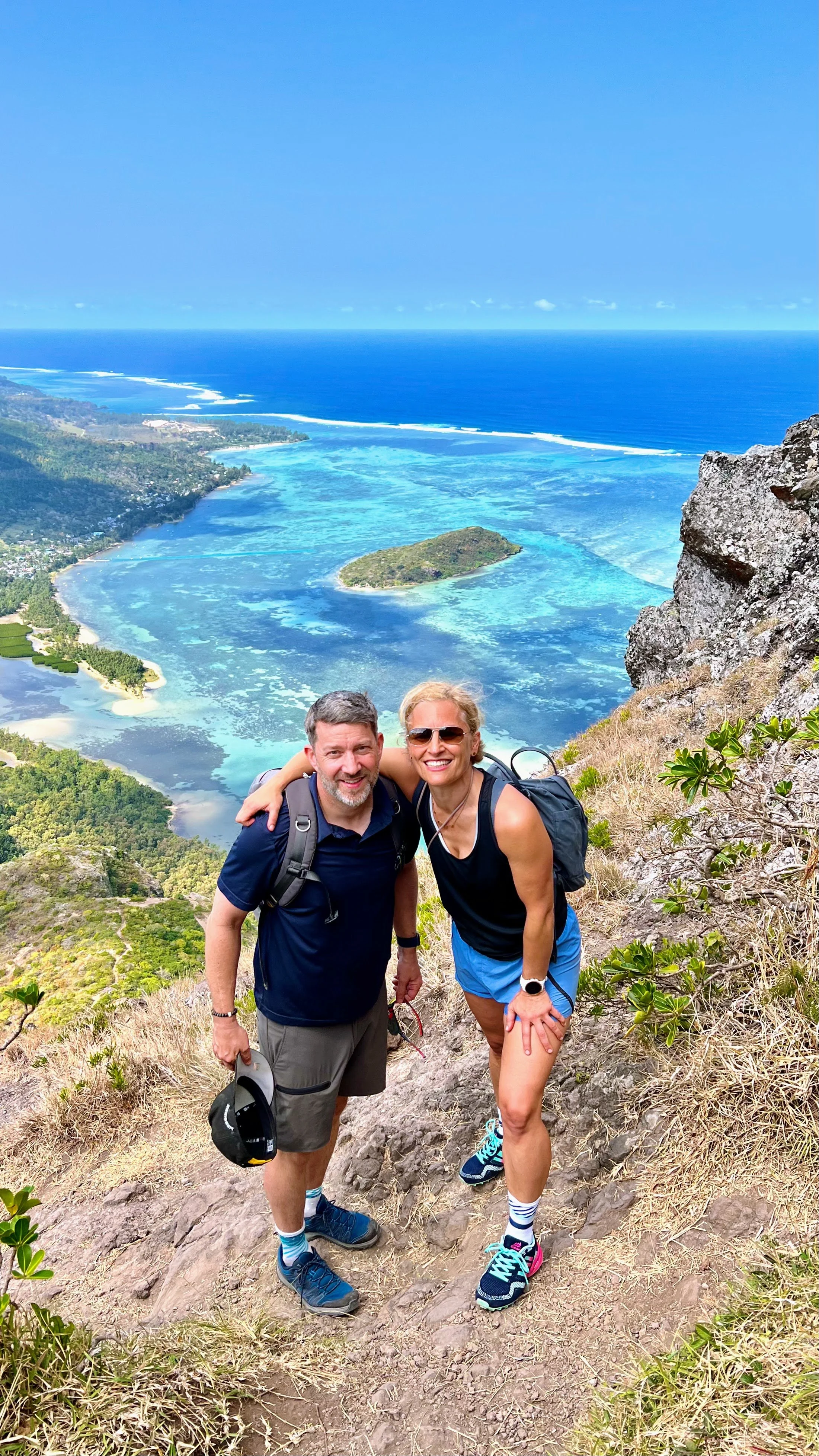A couple standing on a scenic cliff view overlooking lush green islands and crystal-clear blue ocean.