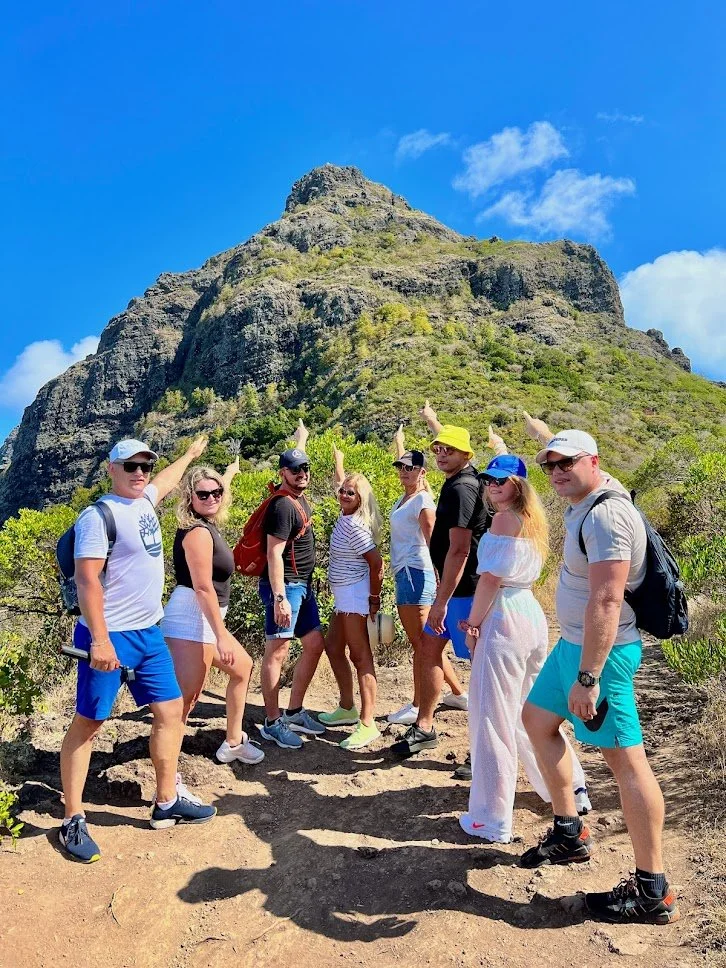 Group hiking on a mountain trail, pointing at the peak with a clear blue sky background.