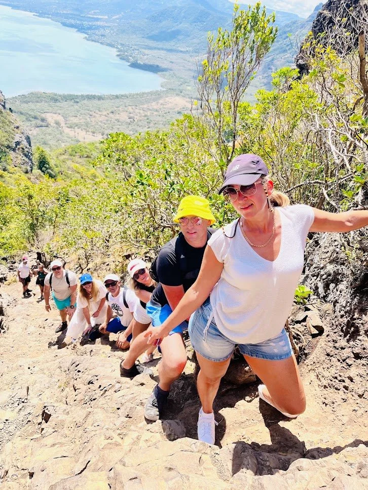 Group of hikers climbing a mountain trail with a scenic view of a lake and landscape in the background.