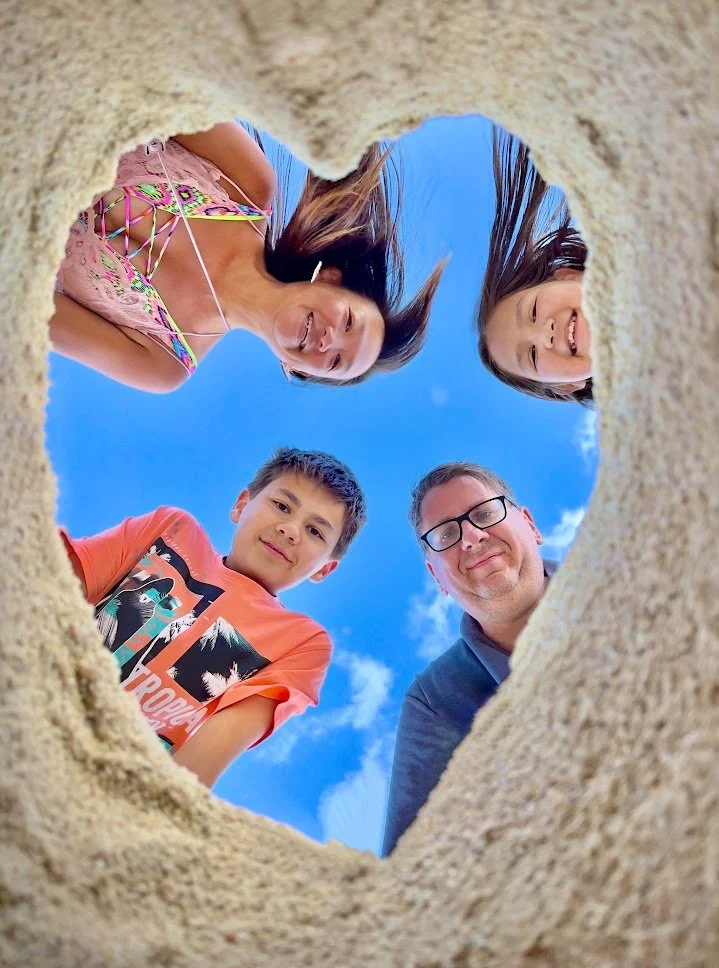 View from a hole in the sand showing people smiling and looking down with blue sky in background.