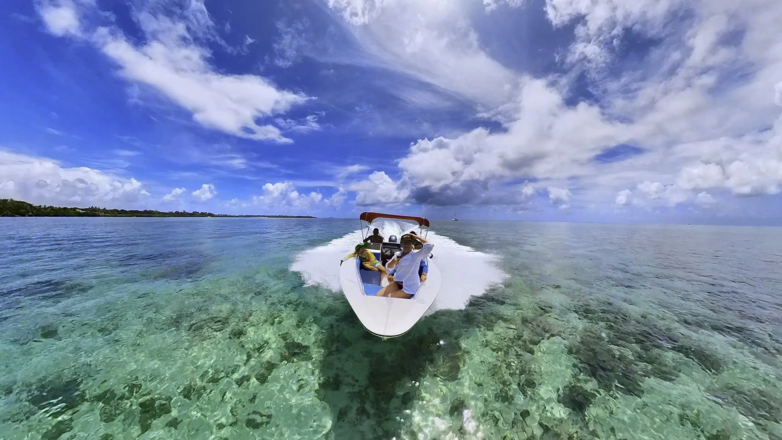 Speedboat with people cruising on clear blue water under a bright sky with clouds.