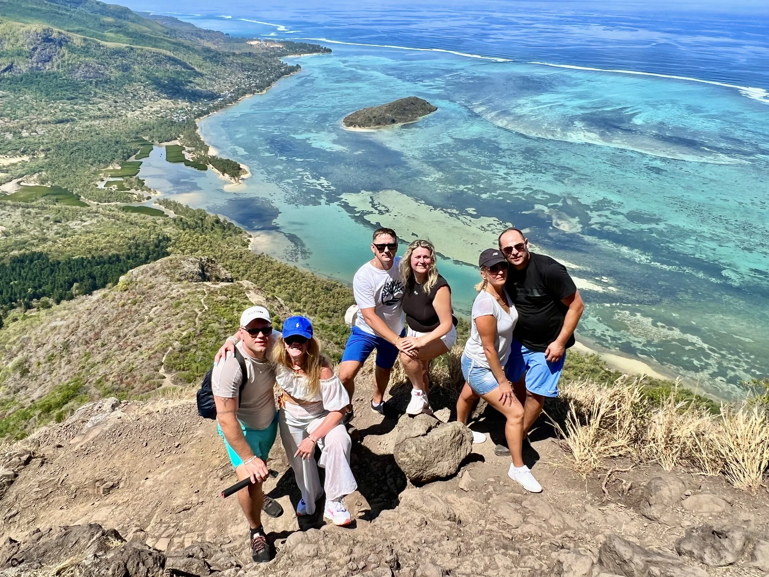 Group on Le Morne Brabant summit overlooking ocean and lagoon in Mauritius, clear blue water, scenic landscape.