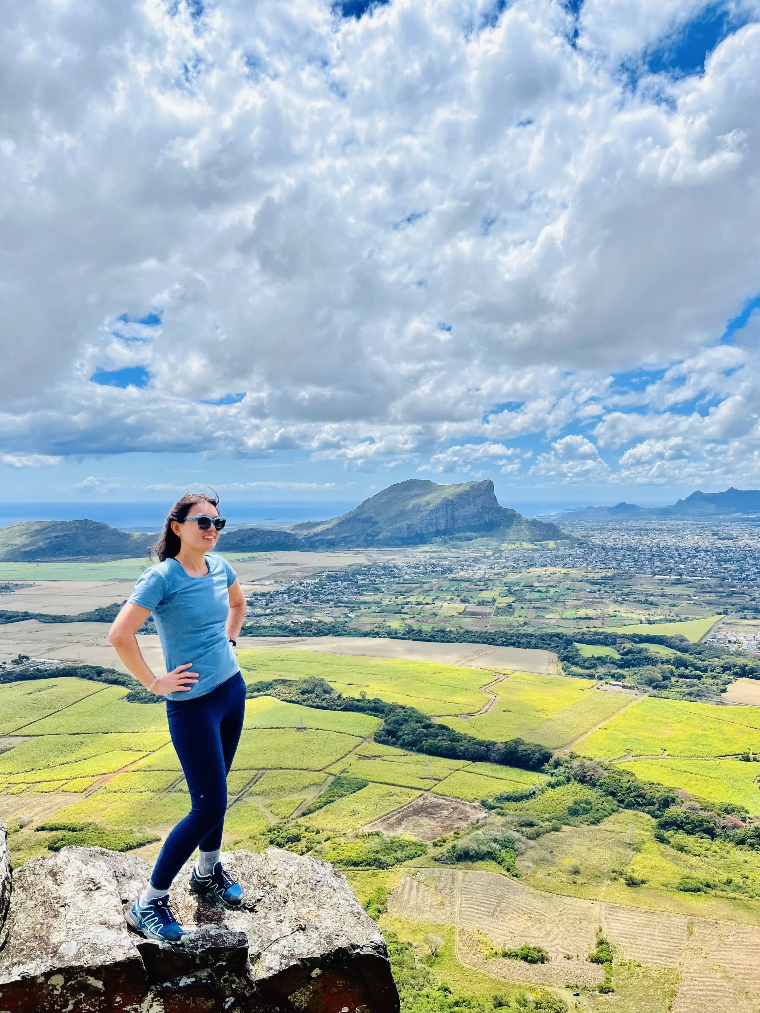 Woman standing on cliff with scenic view of mountains and fields