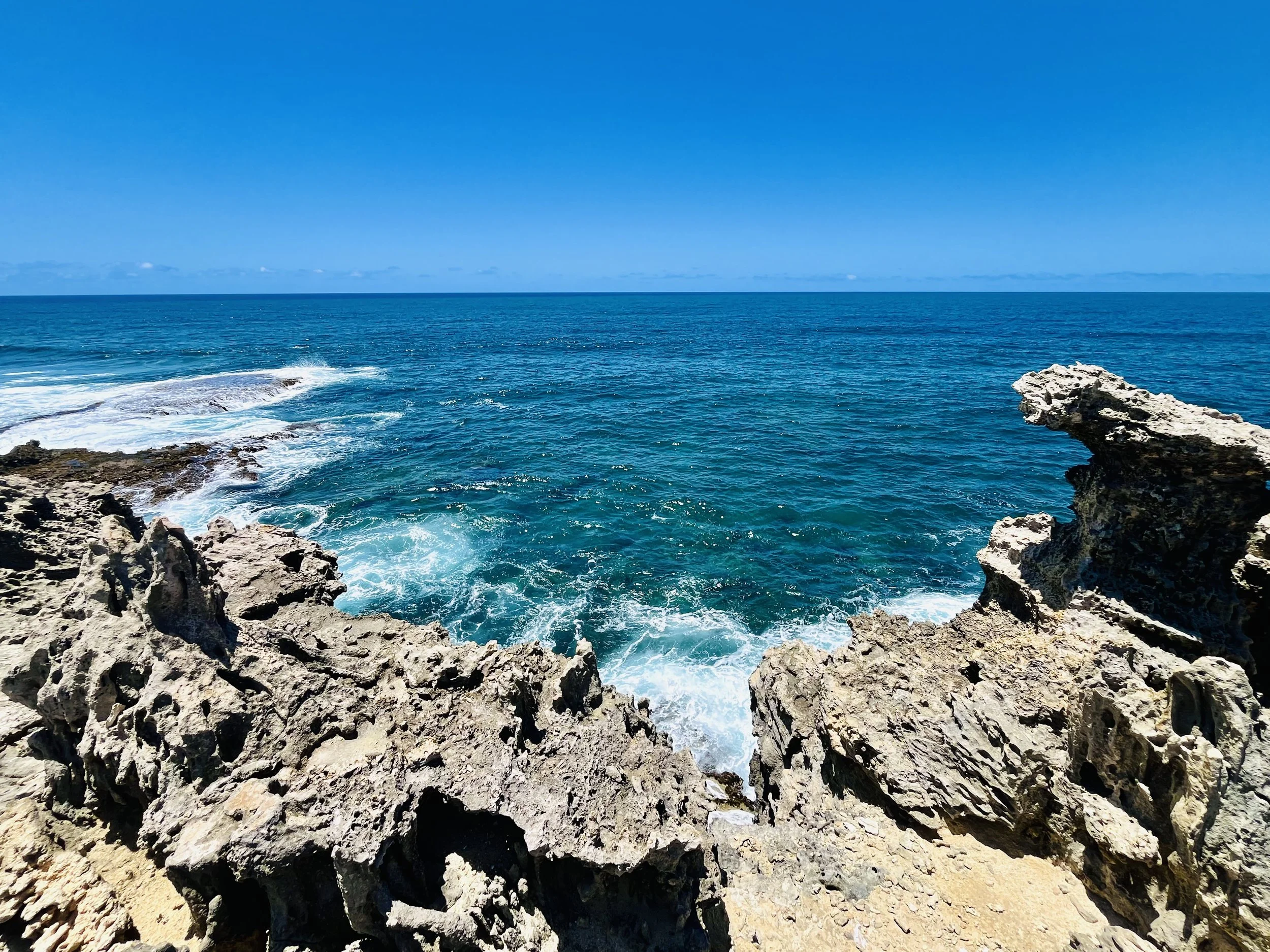 Rocky coastline with ocean waves under a clear blue sky.