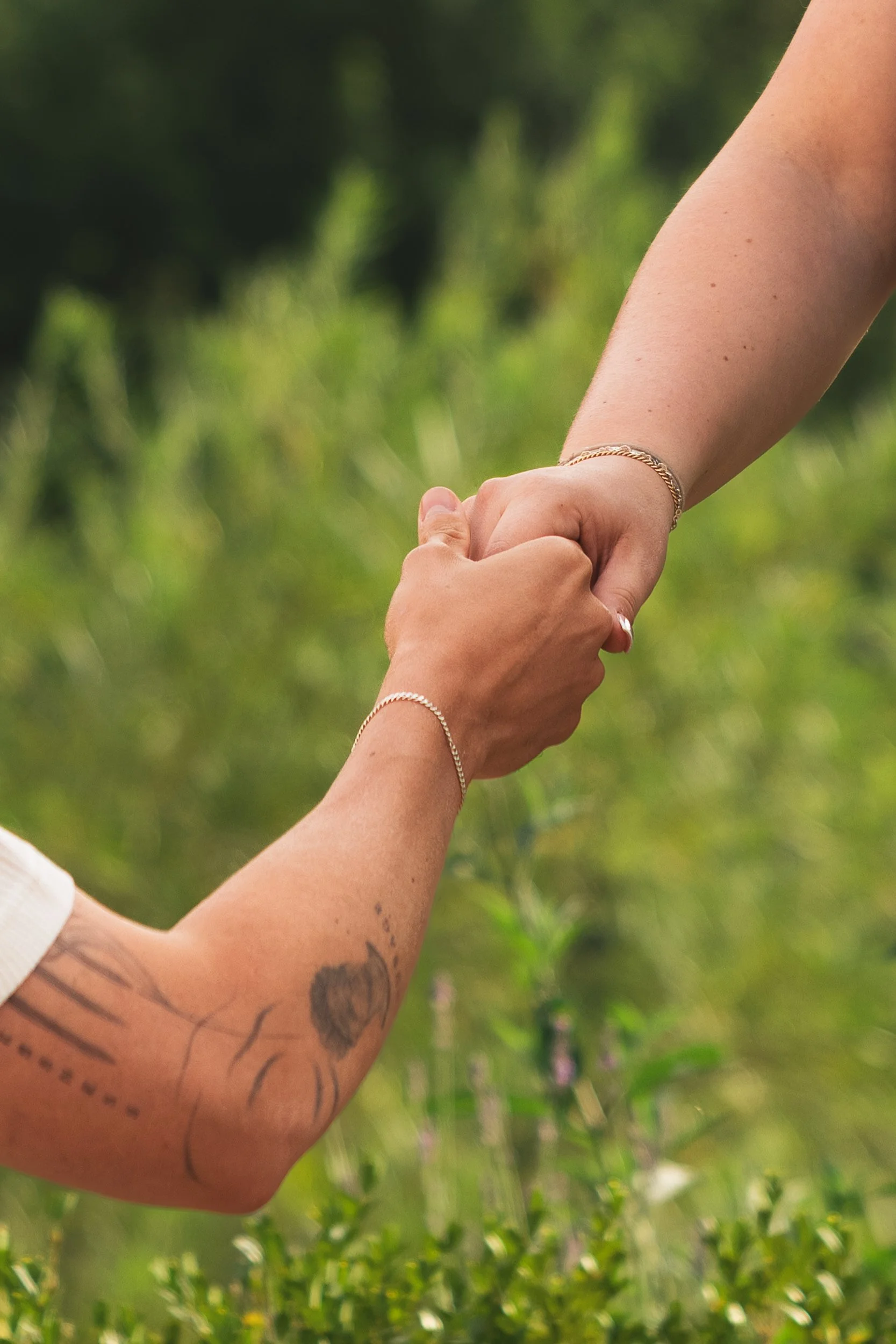 Close-up of two hands holding each other with a blurred green background.