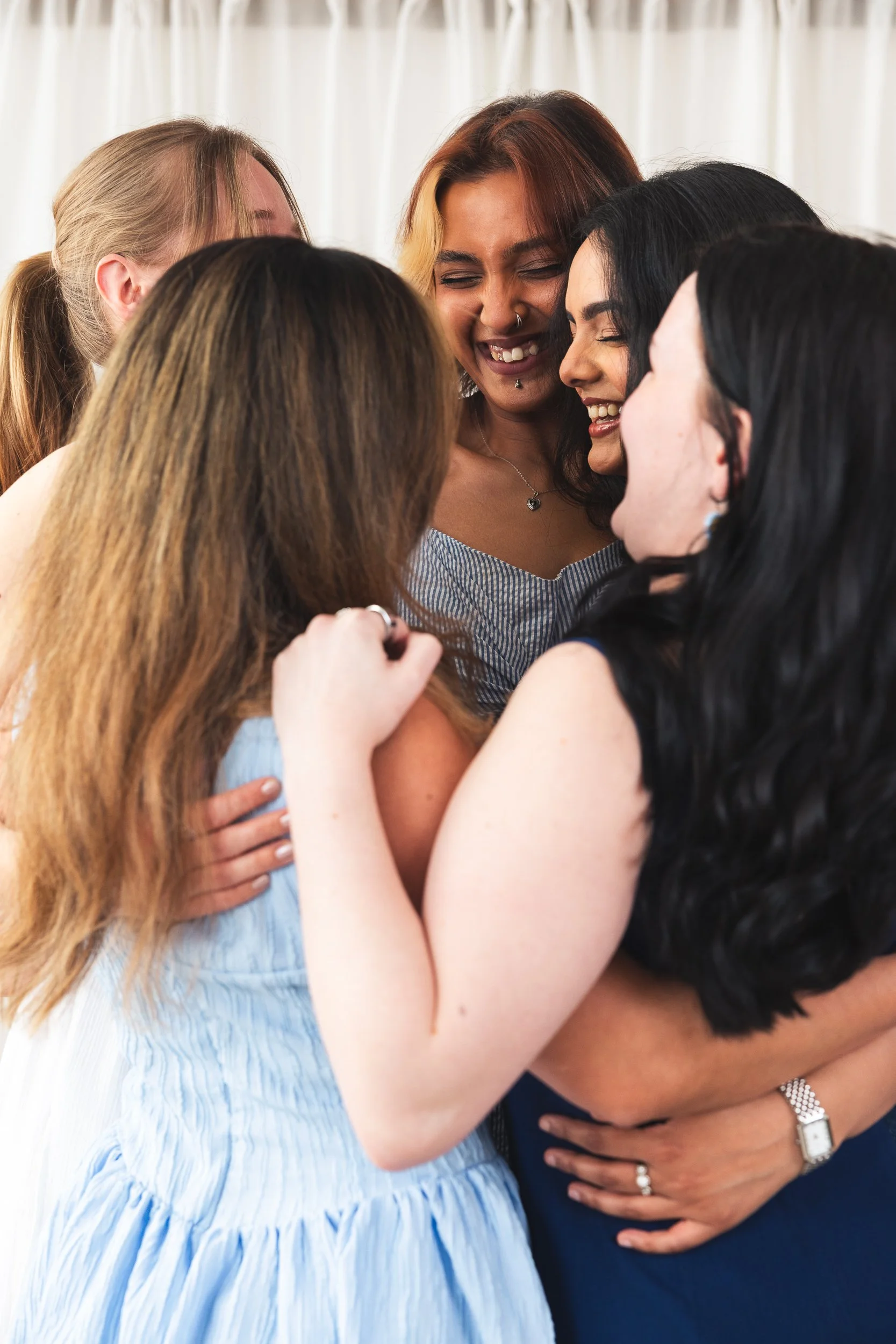 Group of women hugging and laughing together in a close circle, celebrating friendship.