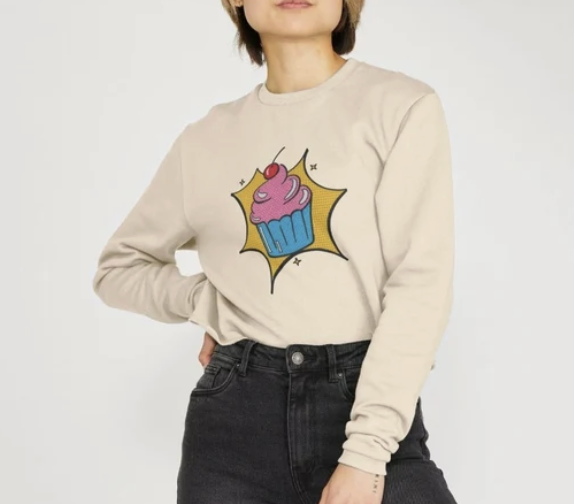 Person wearing a beige sweatshirt with a comic-style cupcake graphic.