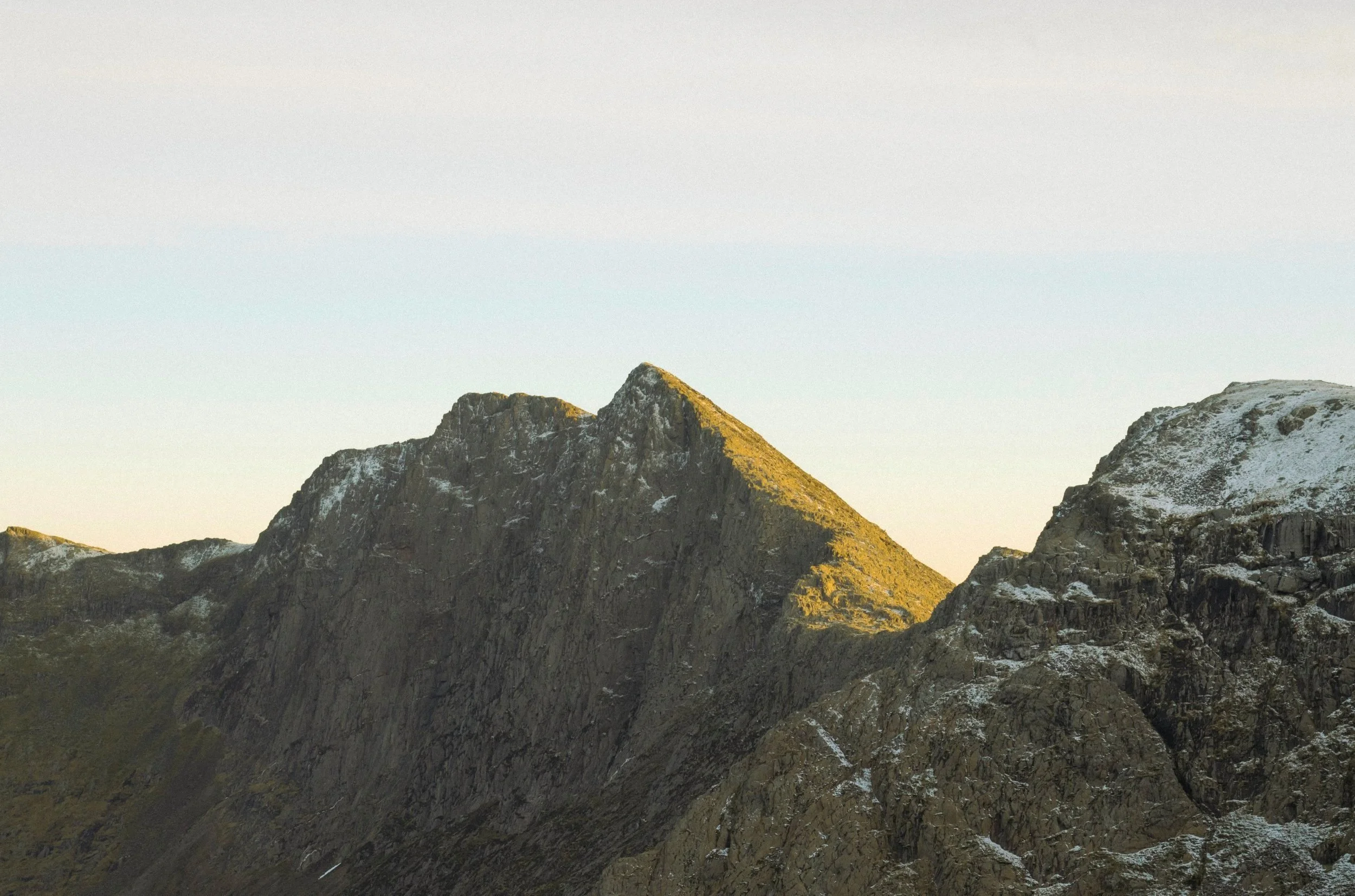 Mountain peaks with some snow and greenery, illuminated by sunlight, under a clear sky.