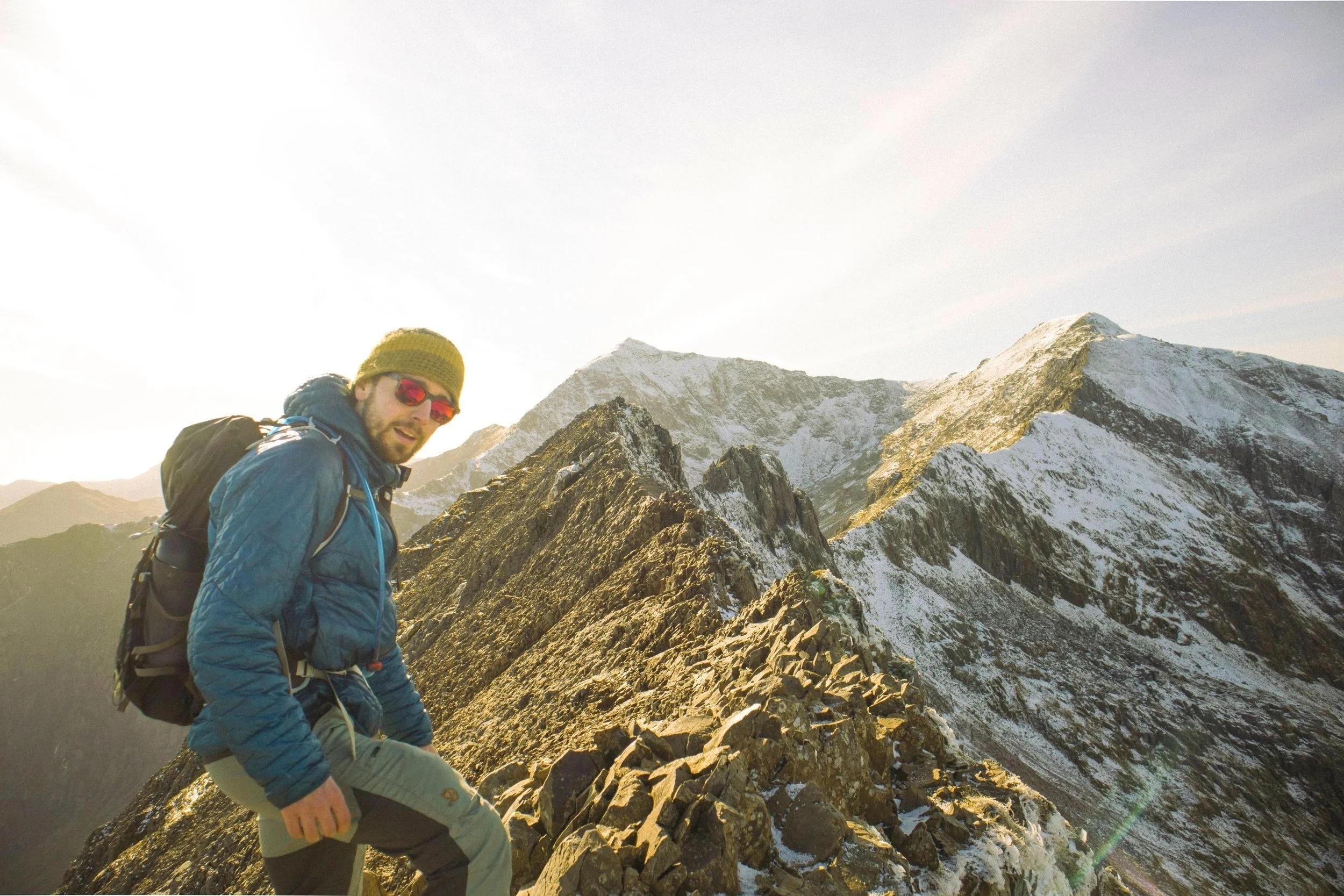 Dom standing on Crib Goch's ridge with snow-covered peaks in the background.