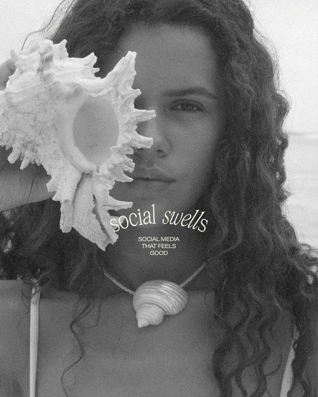 A woman with curly hair holding a large sea shell in front of her face, with a necklace featuring a smaller shell.