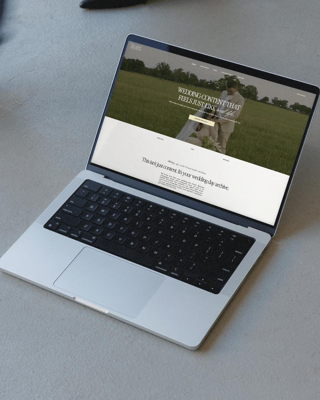 Open laptop on a gray surface displaying a wedding website with a photo of a couple walking in a field.