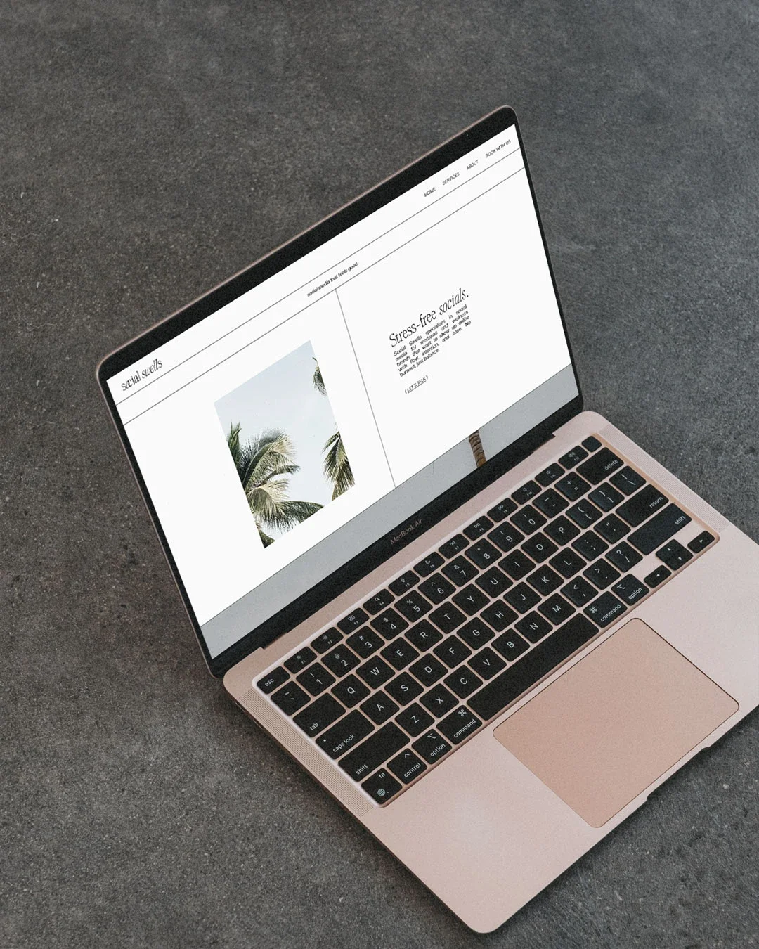 Open MacBook laptop on gray carpet showing a webpage with tropical image and text about social skills and stress-free socials.