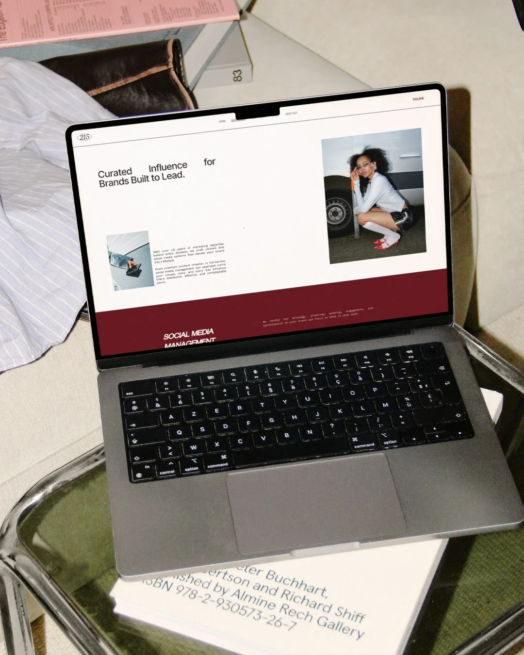 A laptop on top of a book, displaying a webpage about brands and social media management. The webpage includes a photo of a woman squatting beside a white vehicle.