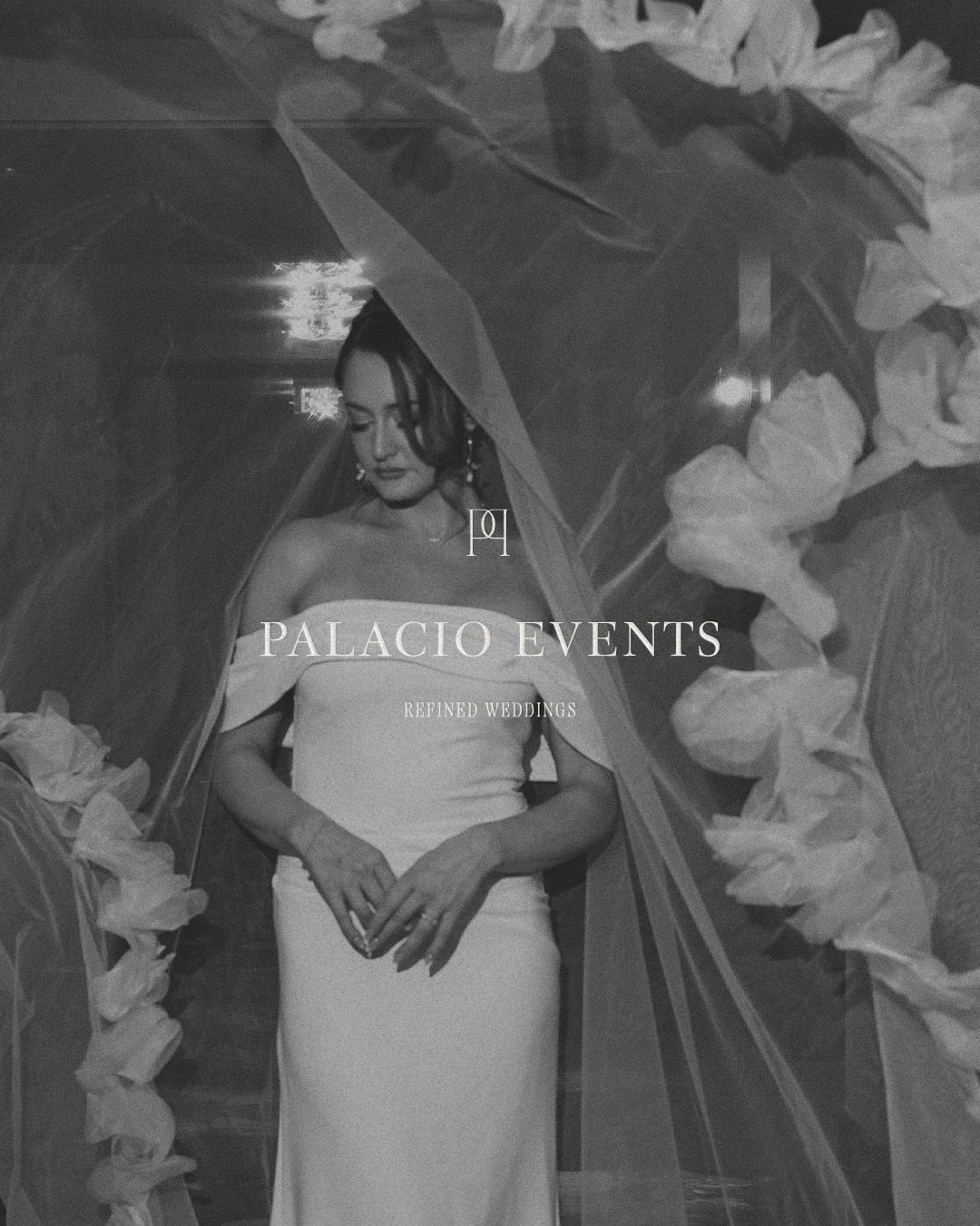 Black and white photo of a woman in a strapless wedding dress, holding her hands together, surrounded by flowers and sheer fabric, with text overlay reading 'Palacio Events, Refined Weddings'.
