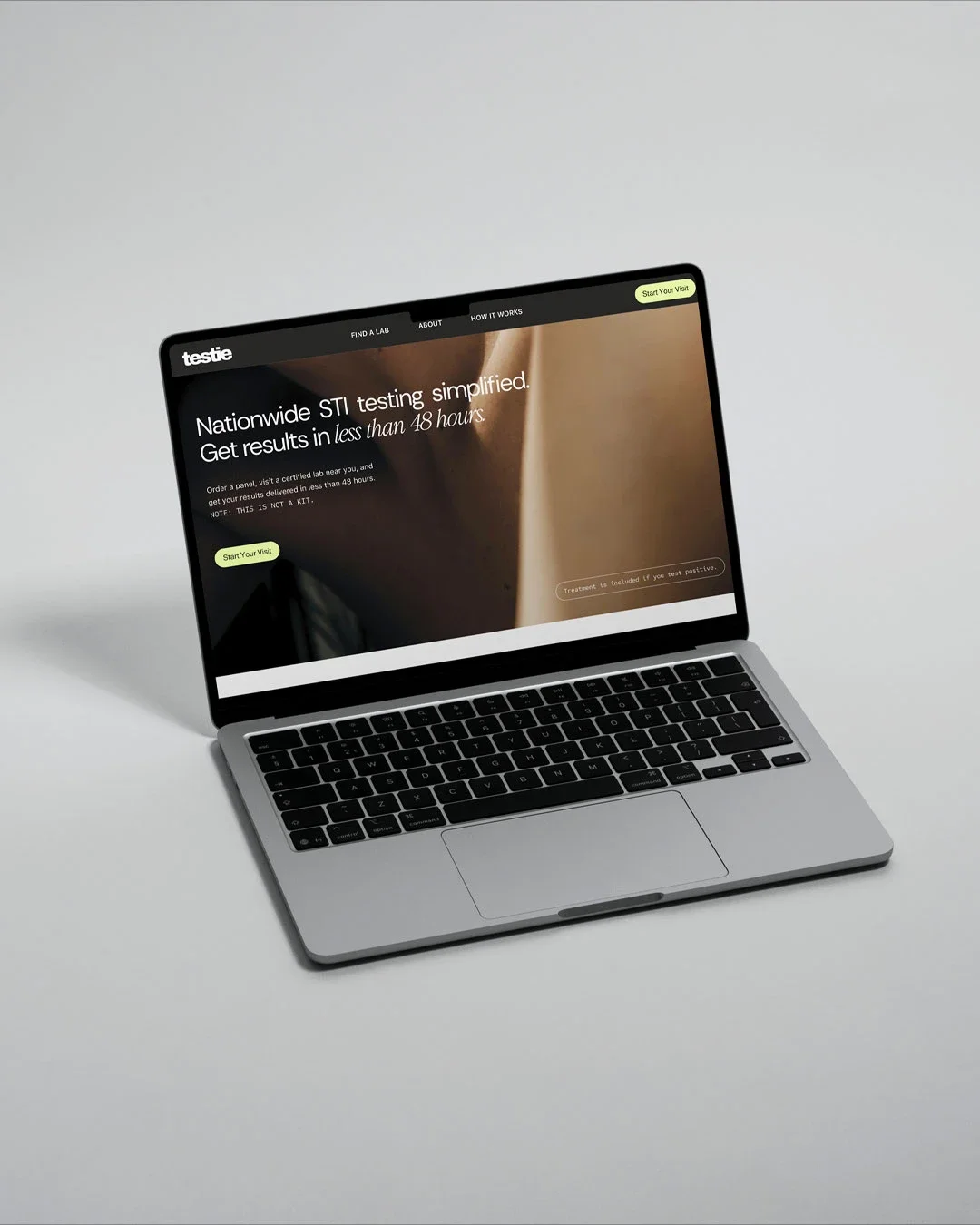 A silver laptop on a white surface showing a website for nationwide STI testing, with the URL 'testie' and options like 'Find a Lab,' 'About,' and 'How It Works,' along with a prominent green button that says 'Start Your Visit.'