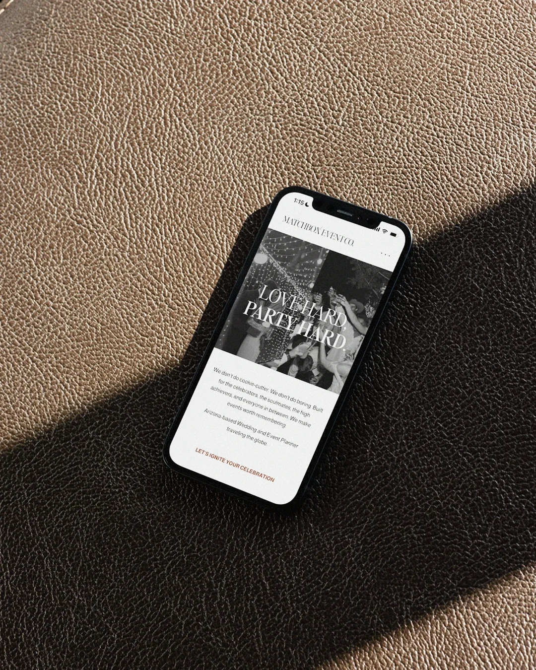 Black smartphone displaying a wedding planning website with pictures and text, lying on a textured brown and black surface.