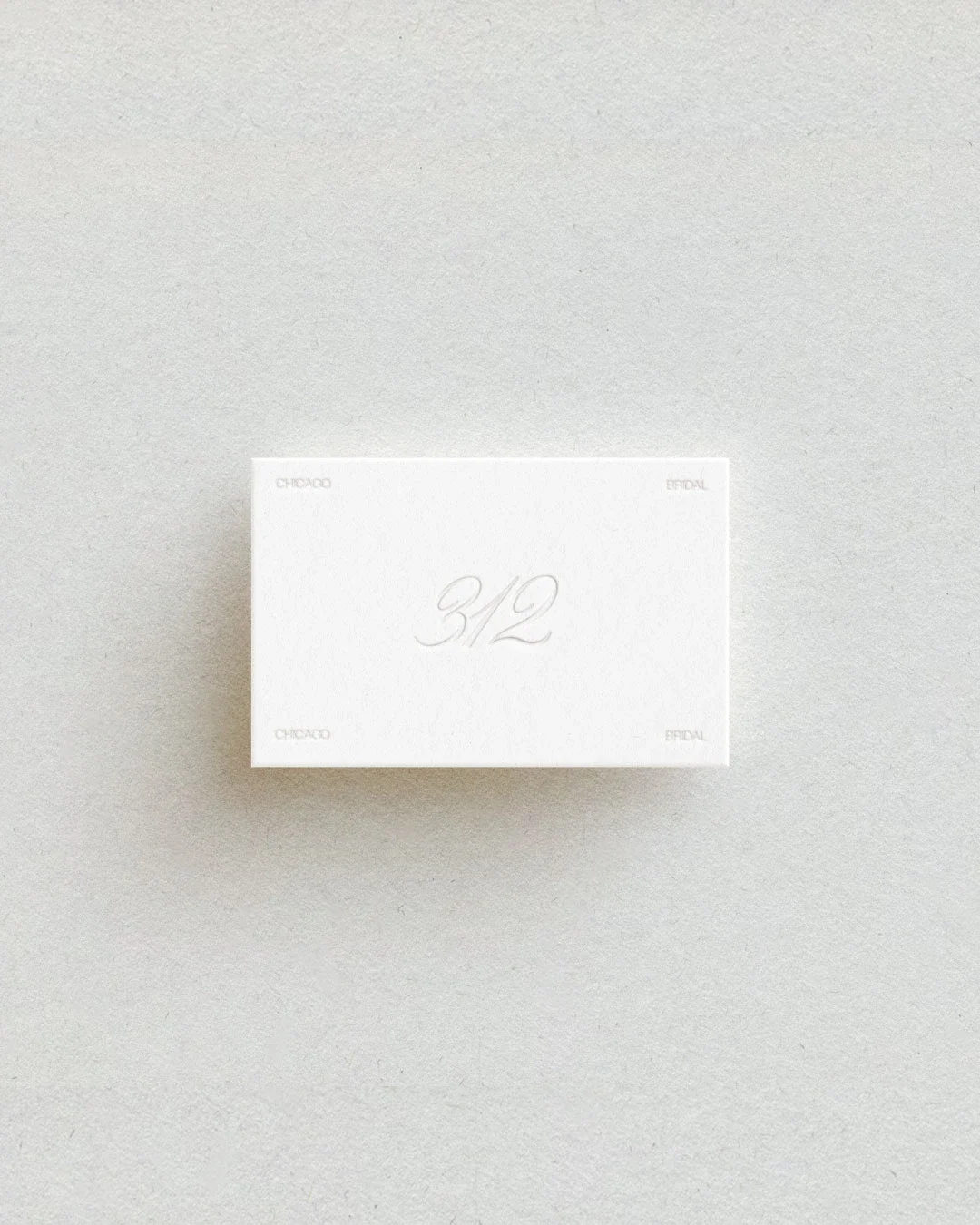 A white box with the number 312 embossed on the top, placed on a light gray textured surface. The box has small text in each corner reading 'Chicago' and 'Bridal'.