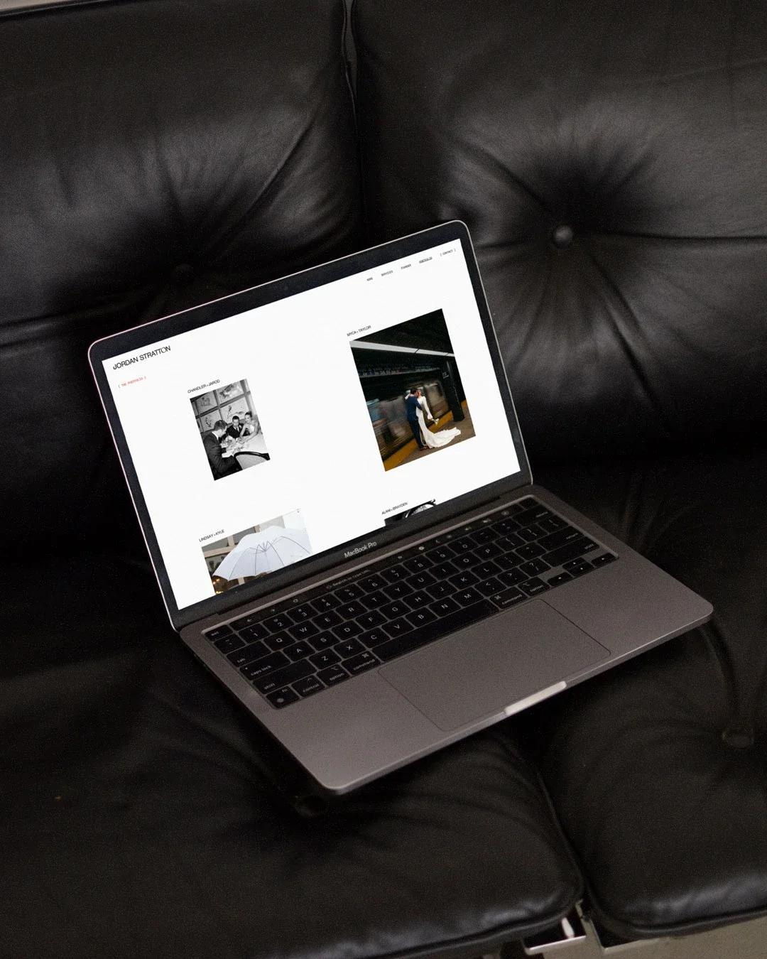 Open MacBook Pro laptop on a black leather couch displaying a website with photos and text.