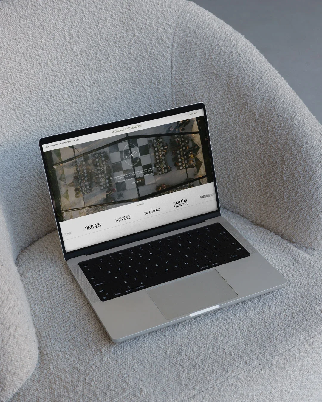A MacBook laptop on a textured beige armchair with a wedding planning website open on the screen.