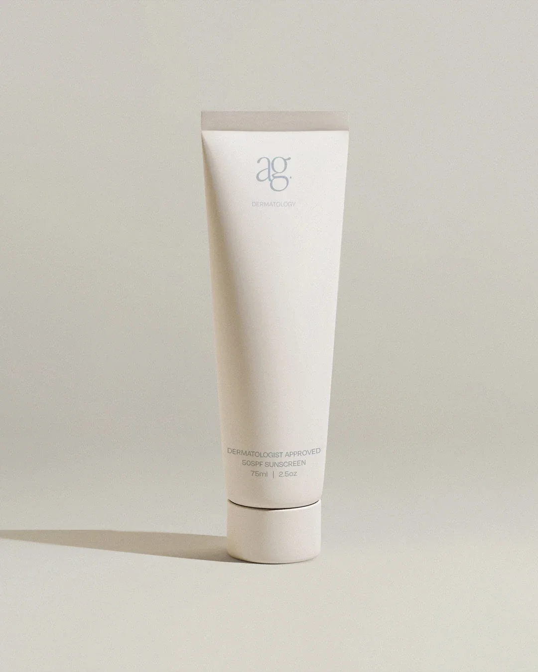 A white tube of skincare product labeled 'ag DERMATOLOGY' standing upright on a light surface with a plain background.