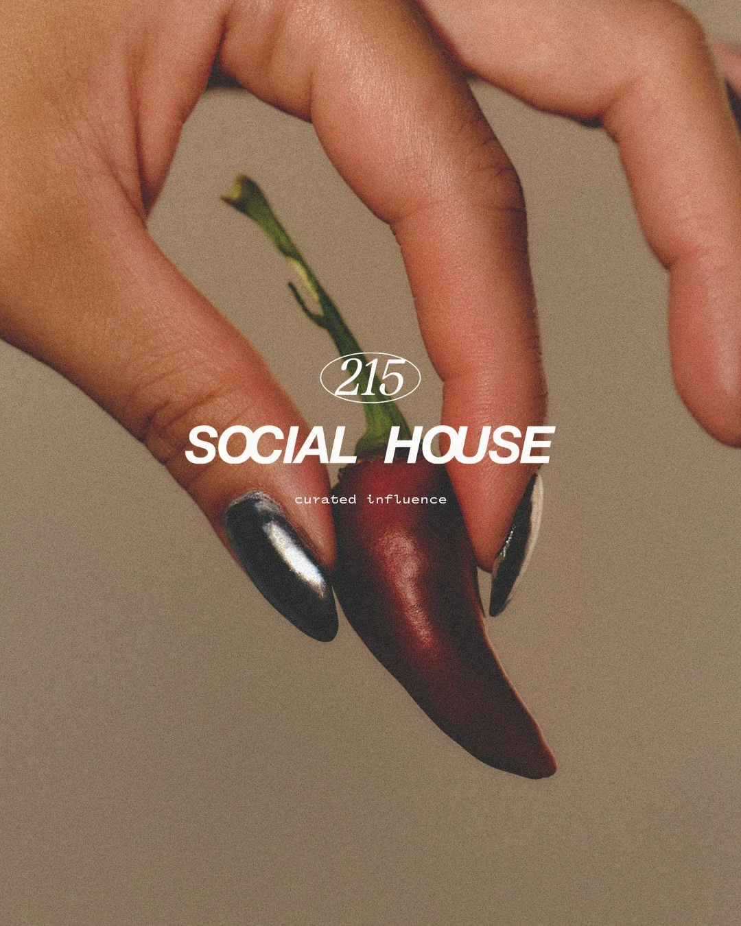 A hand with metallic black and silver nails holds a red chili pepper with a green stem. Overlaid text reads '215 SOCIAL HOUSE curated influence'.