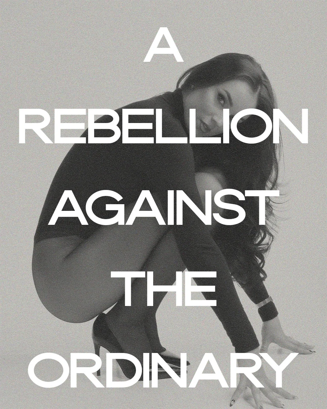 Black and white photo of a woman wearing high heels in a crouched position with her head tilted to one side and her mouth slightly open. Overlaid text reads: 'A REBELLION AGAINST THE ORDINARY.'