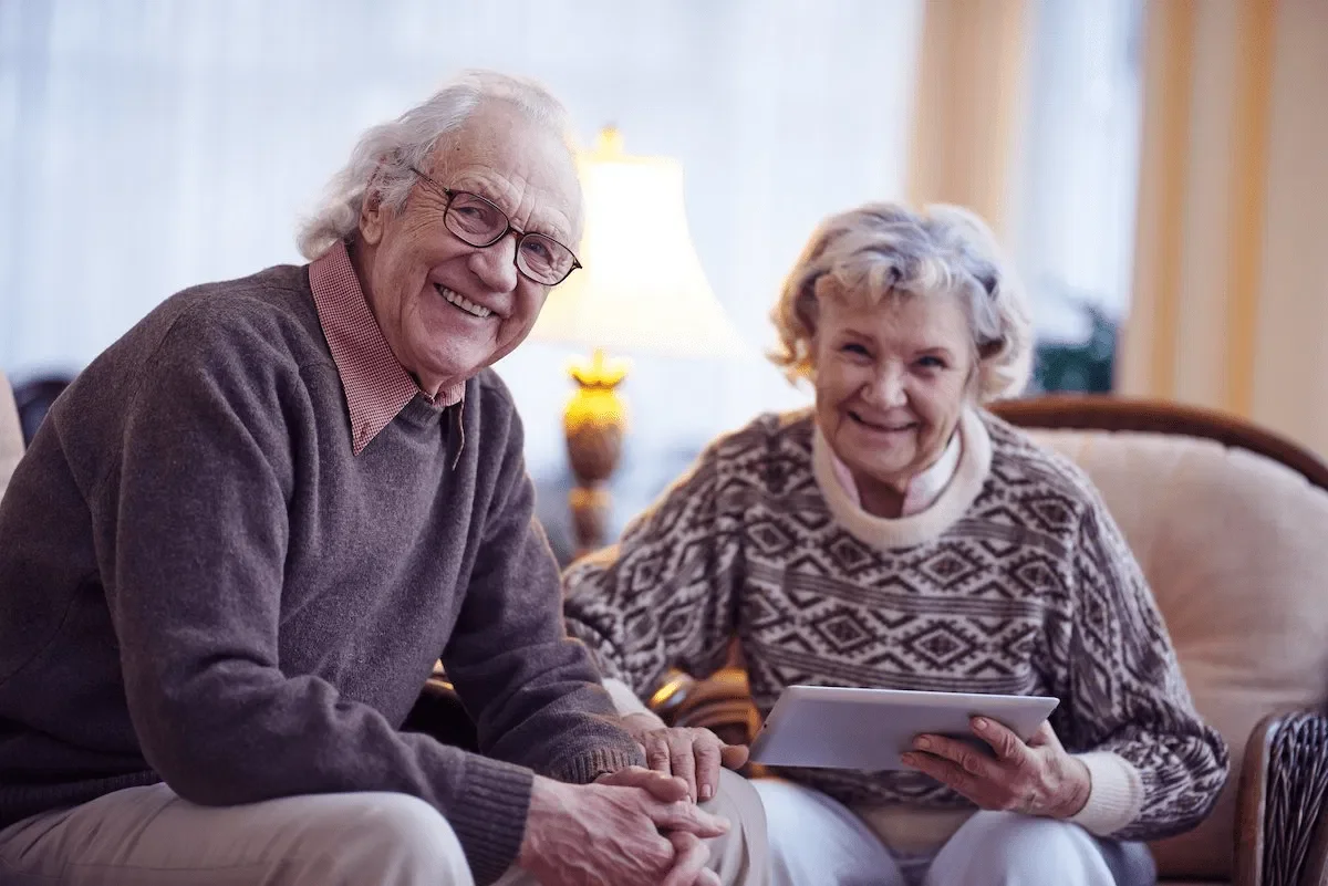 An older couple sits together in a warmly lit, cosy lounge, smiling and relaxed