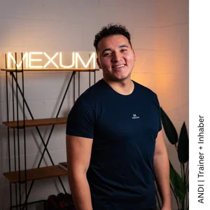 Andi, Trainer und Inhaber des Motus Sportstudios, im Studio vor einer beleuchteten MEXUM-Schrift