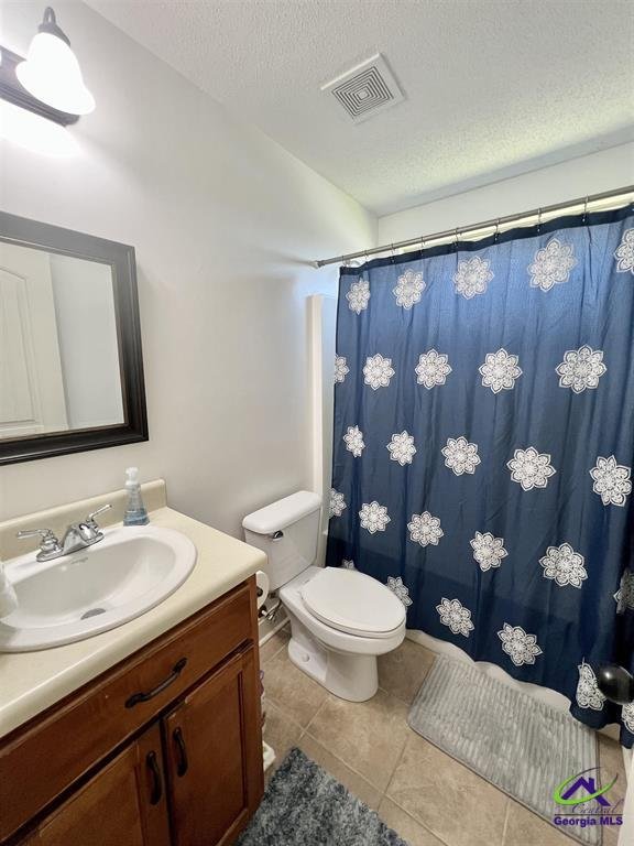 Bathroom with a sink and a wooden cabinet, toilet, and a shower with a blue curtain featuring white floral patterns.
