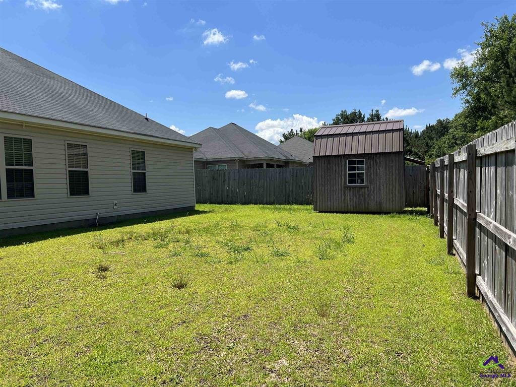 Backyard with grass, wooden fence, a small shed, and part of a house.