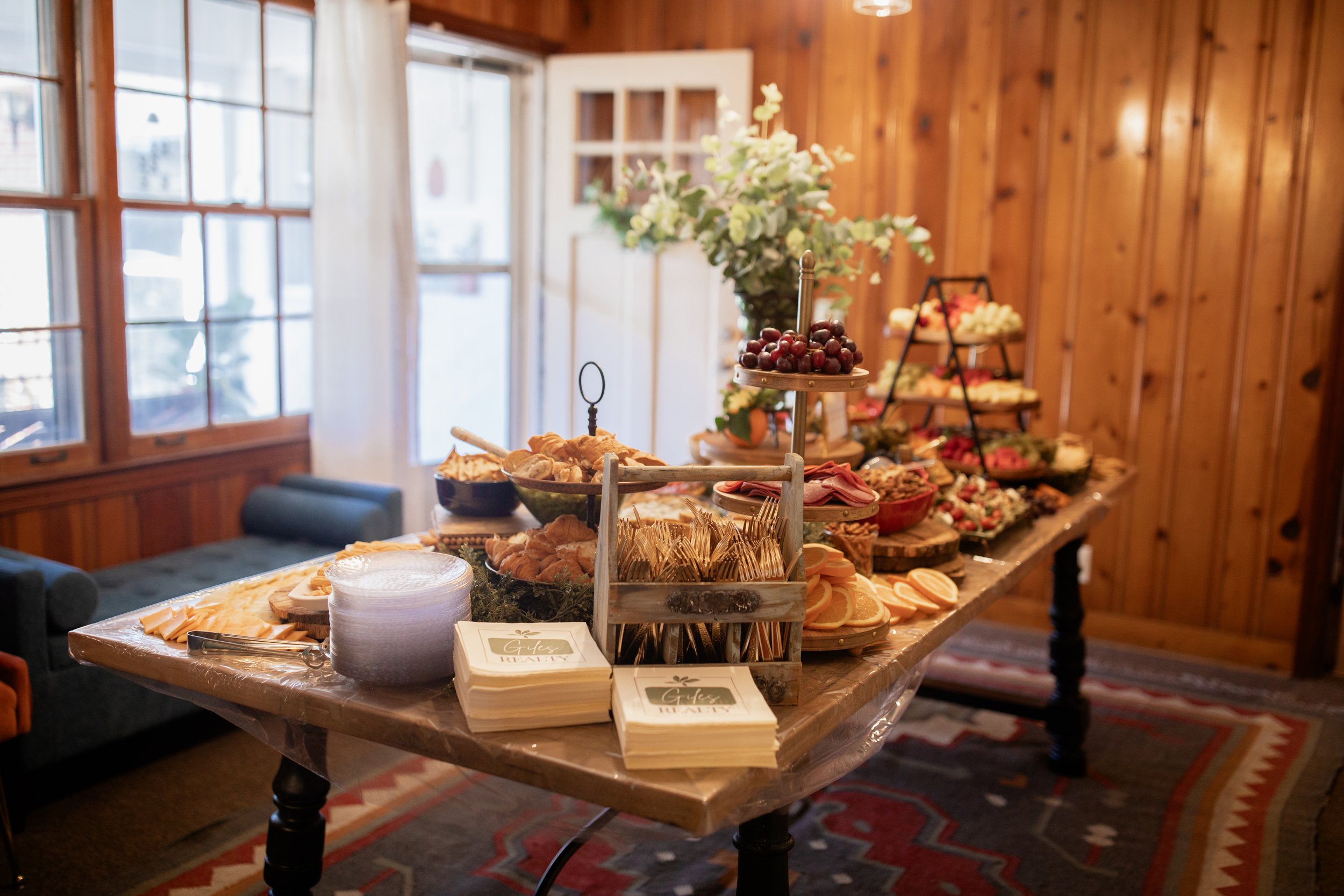 Buffet table with assorted food items, including fruit, pastries, and utensils in a rustic room with wood paneling.
