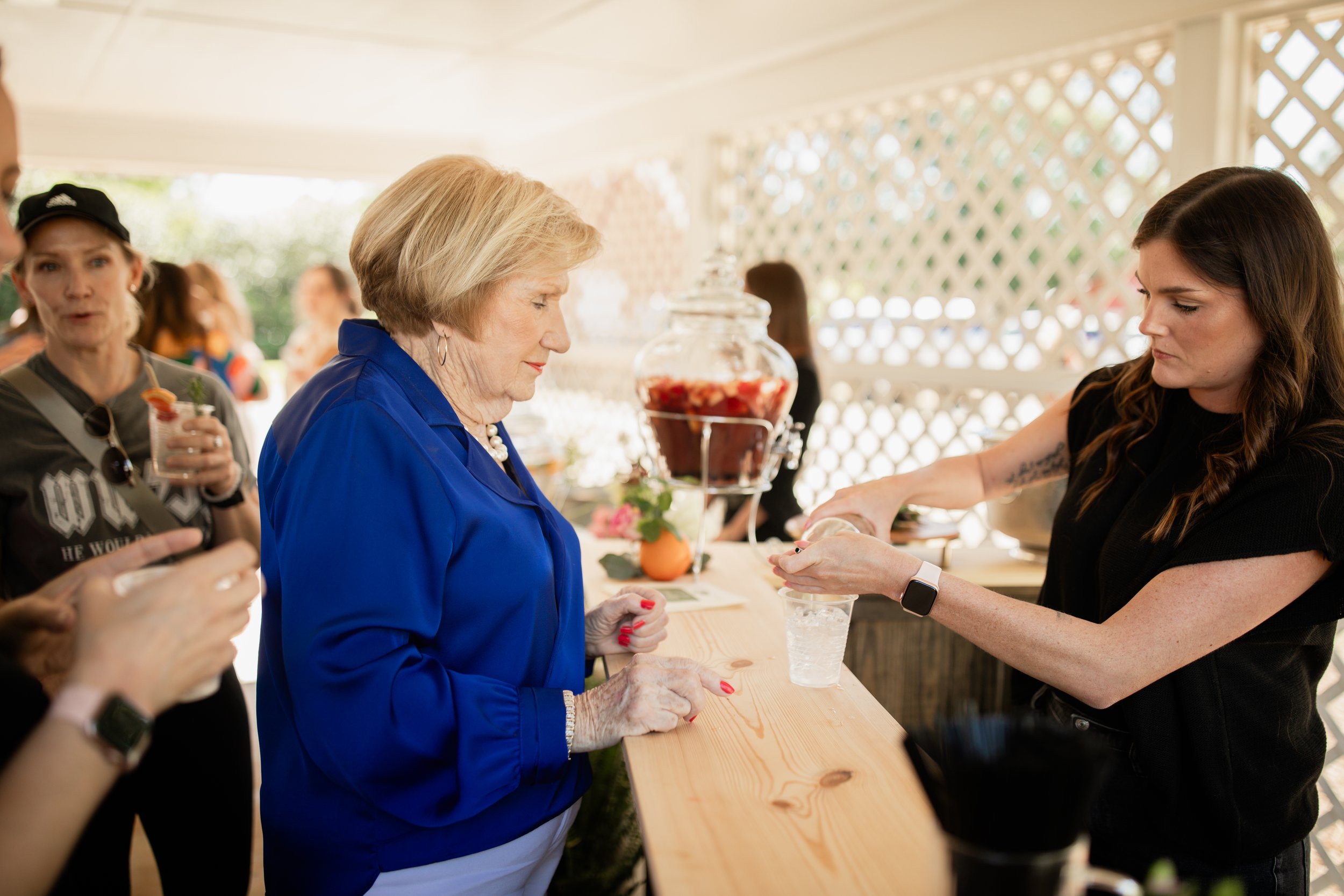 Woman at a wooden counter attending to a customer at an outdoor event, with drinks and decorations visible.