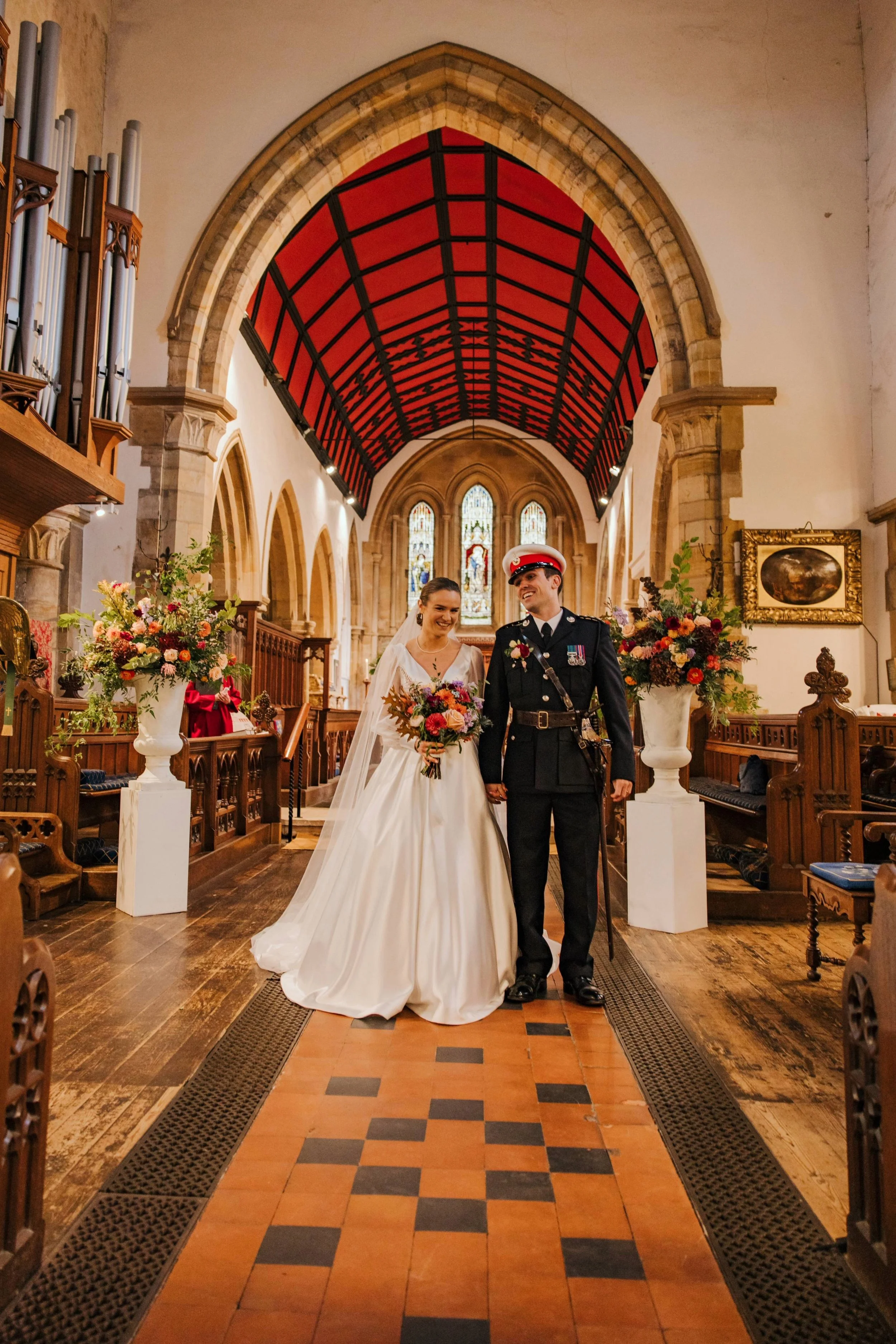 Wedding couple stood in church with a large urn of flowers either side of them 