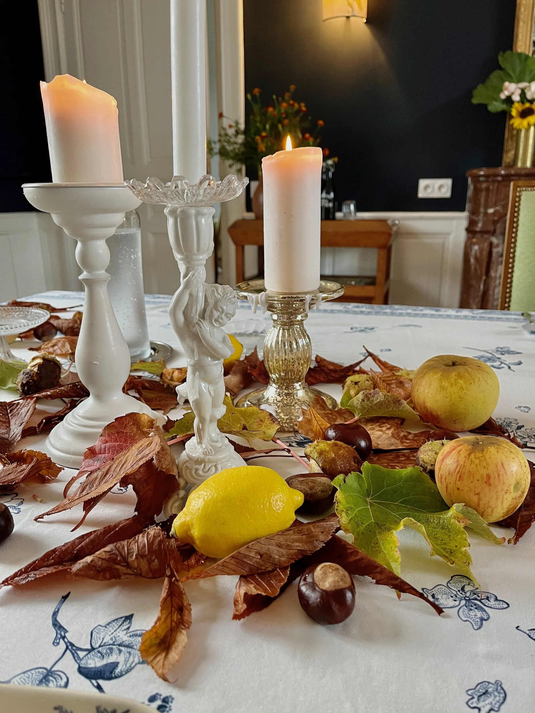 A table centerpiece with lit candles, a lemon, apples, and decorative leaves.