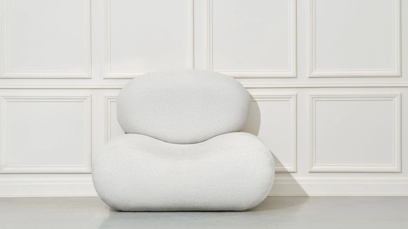 A white modern, rounded armchair placed against a white paneled wall in a minimalistic room.