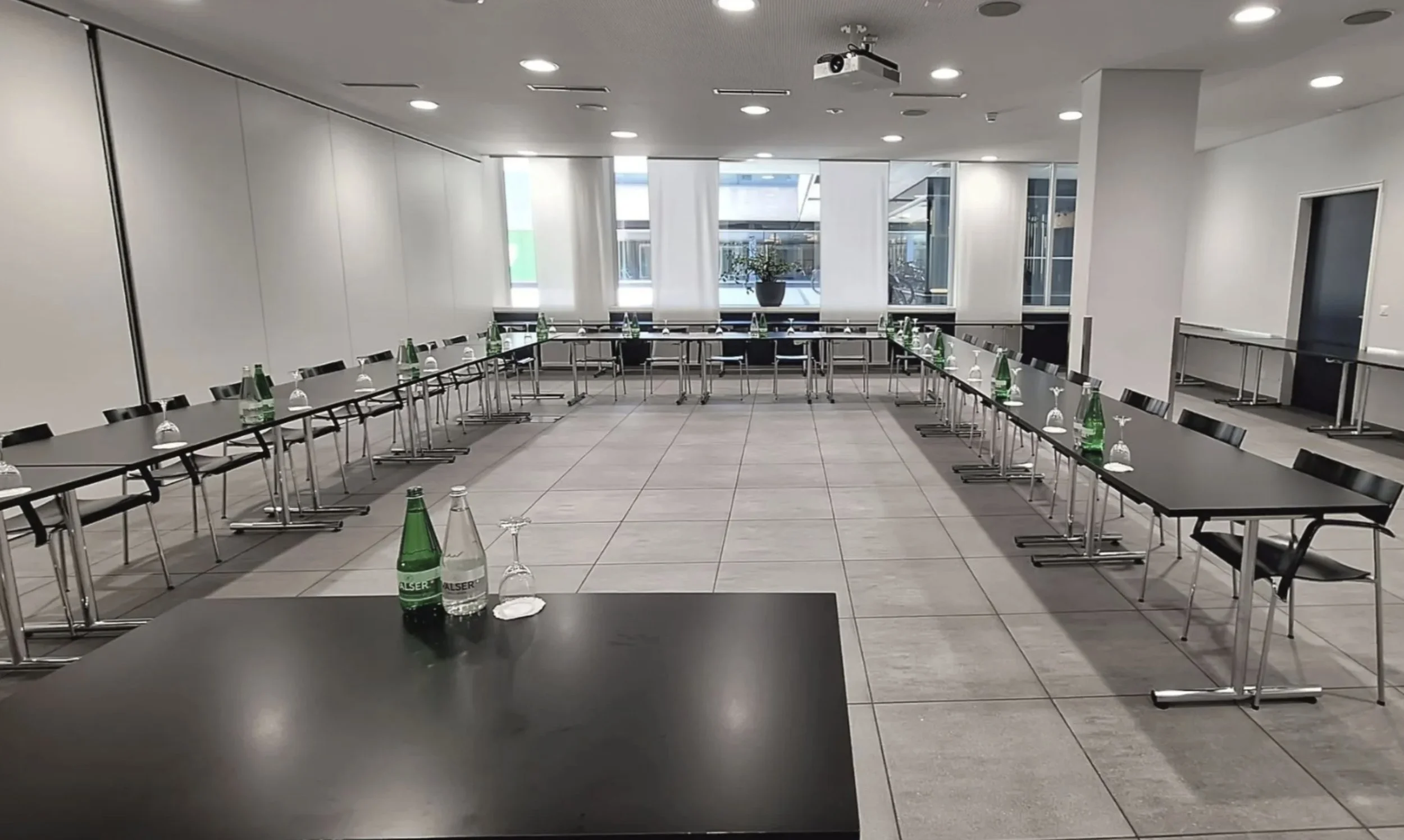 Seminarraum vor dem Workshop: Tische in U-Form, auf jedem Platz eine Flasche Mineralwasser und ein Glas