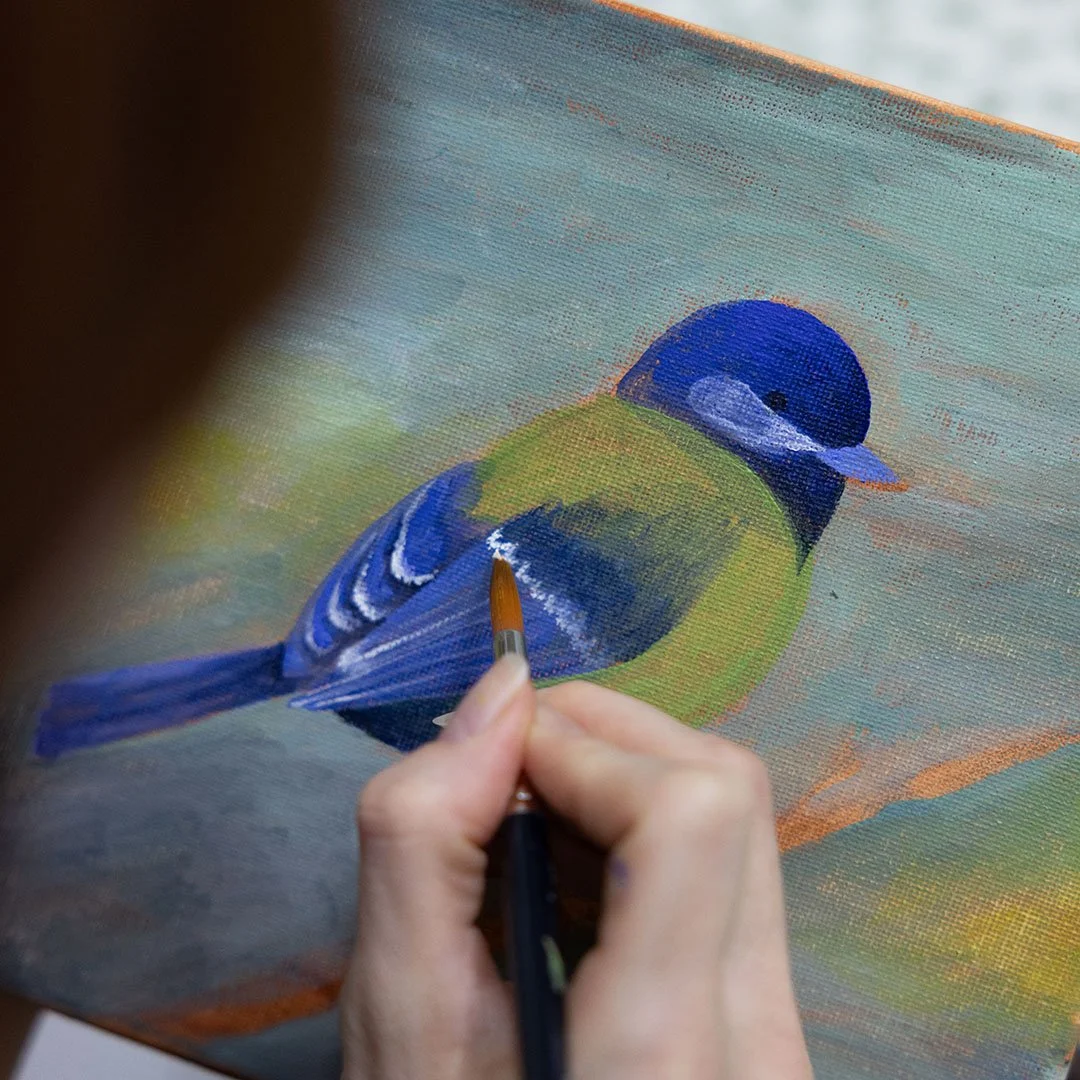 Una persona che dipinge un uccello di digitale su una tela con un pennello.