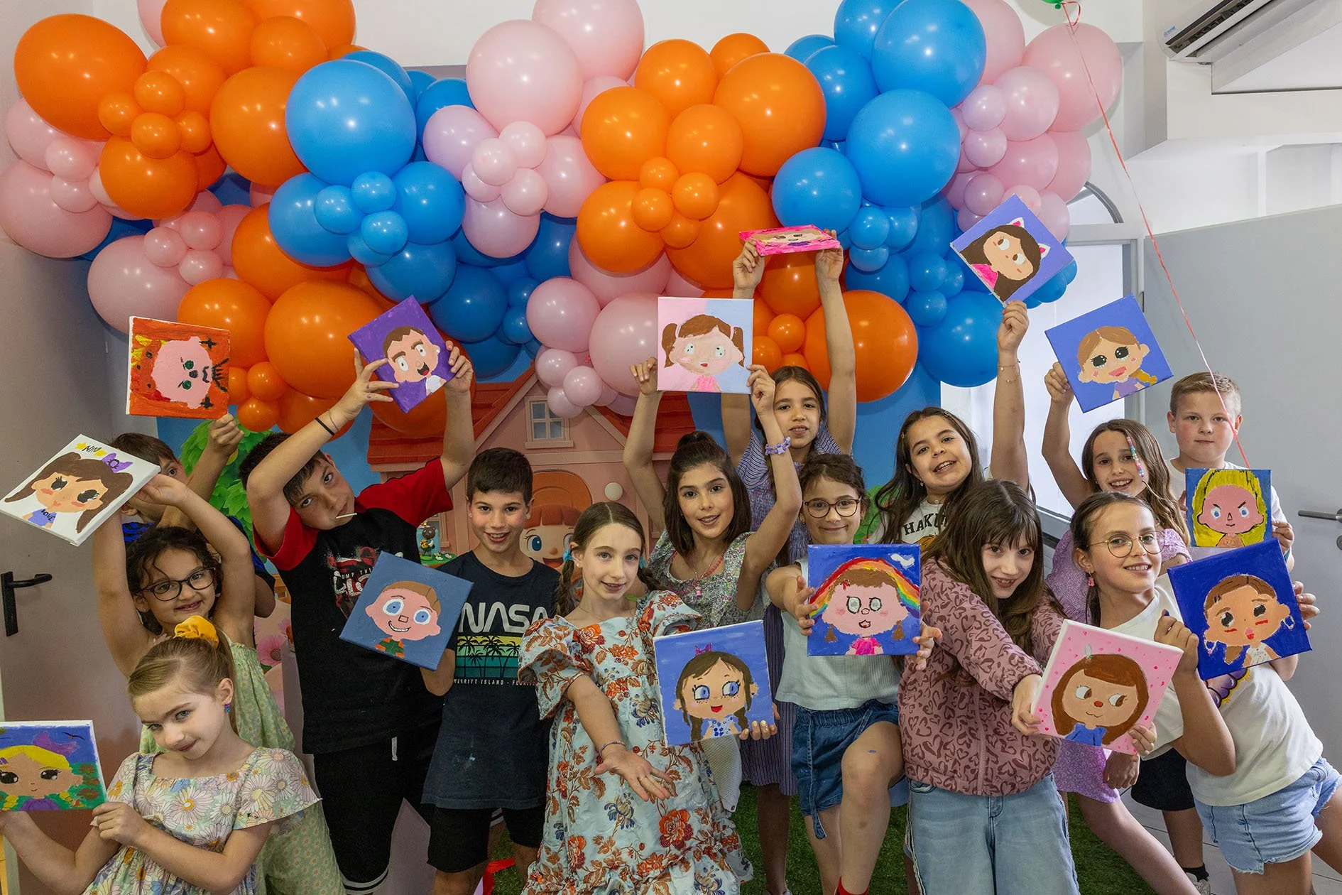 Gruppo di bambini felici che mostrano disegni fatti a mano, con decorazioni di palloncini colorati sullo sfondo.