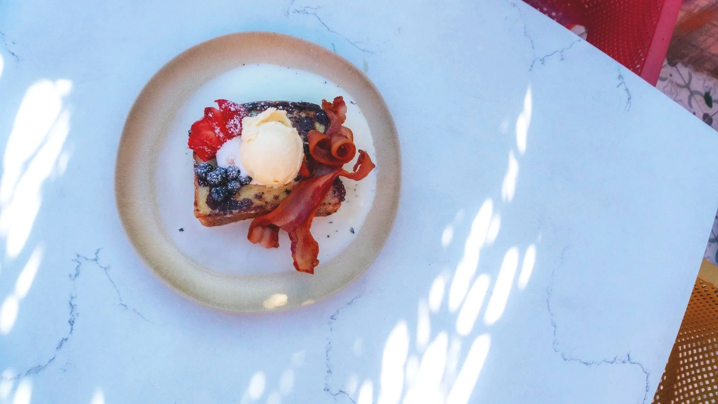 Dessert with a scoop of vanilla ice cream, berries, crispy bacon, and whipped cream on a plate