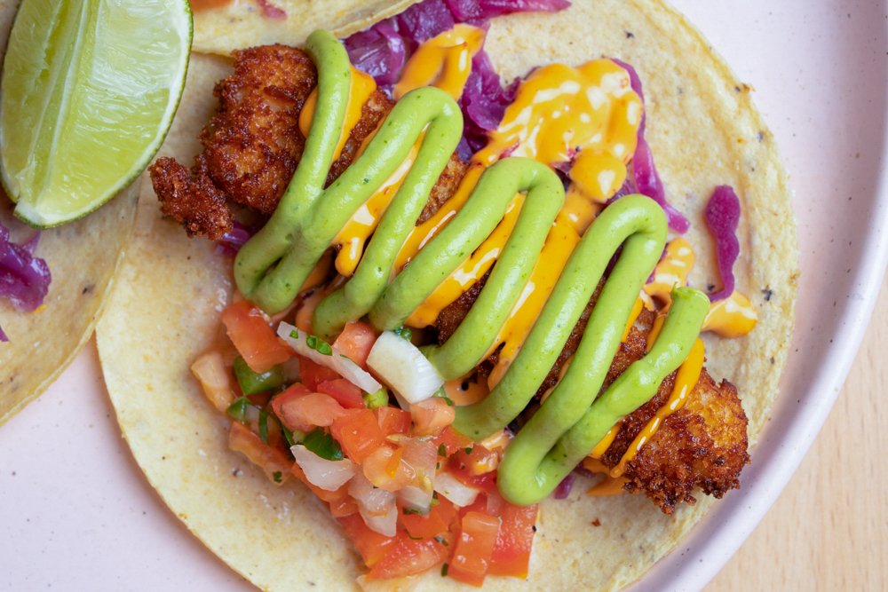 Close-up of two Mexican tacos on a plate, topped with chopped onions, and served with a lemon wedge.