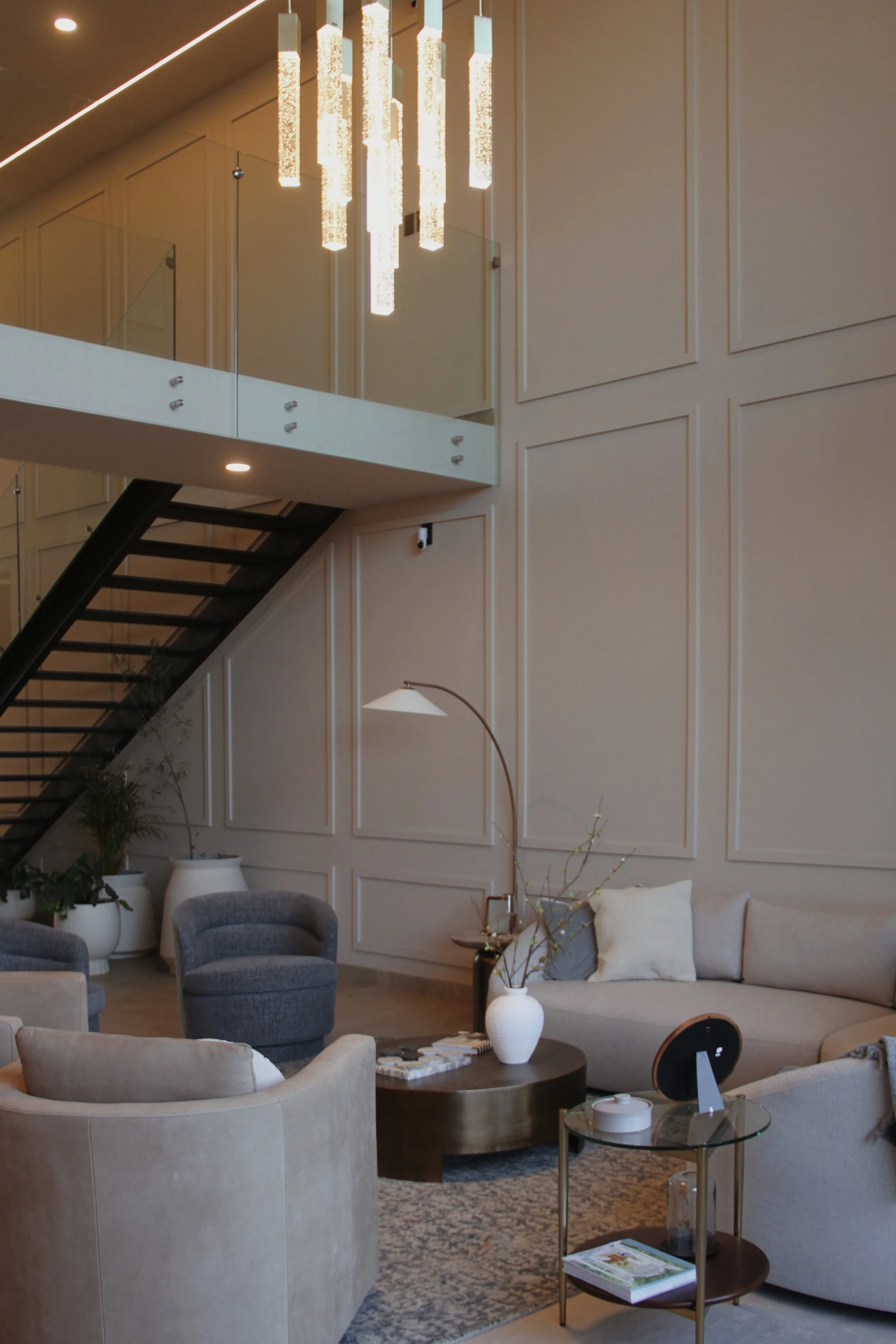 Sala de estar con sillones en tonos neutros, una mesa de centro y plantas en macetas grandes, decorada con un estilo moderno y elegante.