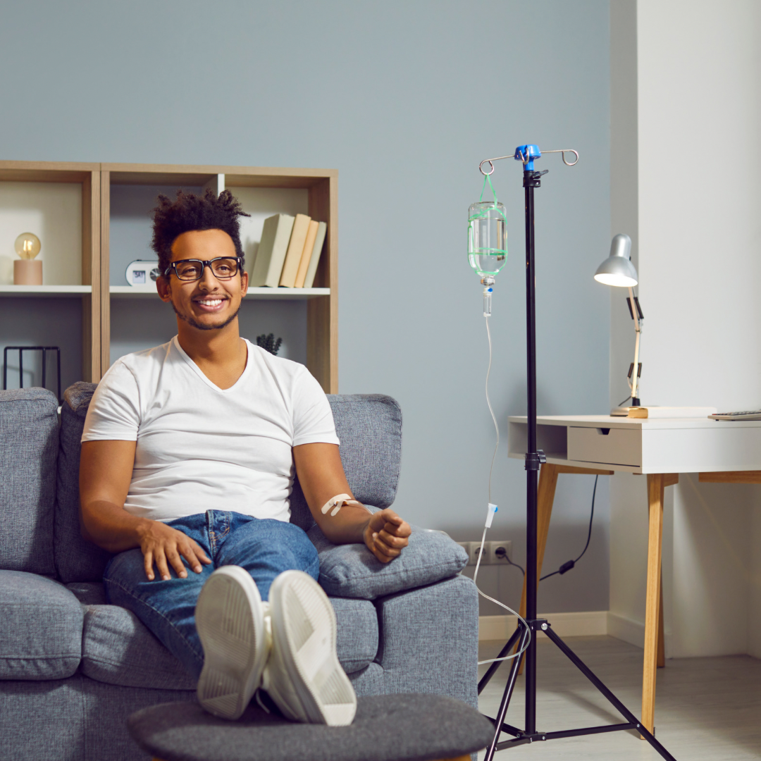 A young man smiles, sitting on the couch with his feet up as he received IV therapy.