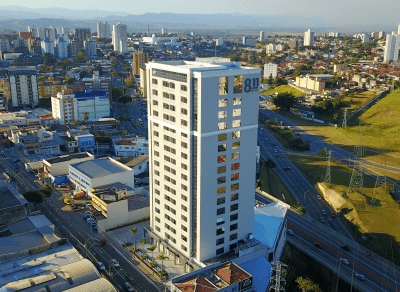 Prédio moderno, do escritório da MBR, em uma área urbana com várias construções e uma rodovia nas proximidades, visto de cima ao pôr do sol.
